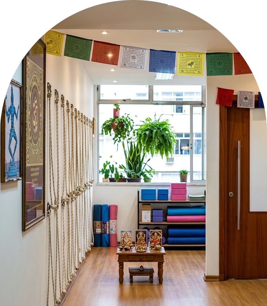 Corredor do estúdio Ananda com cordas de yoga na parede, bandeiras coloridas e a janela com plantas ao fundo